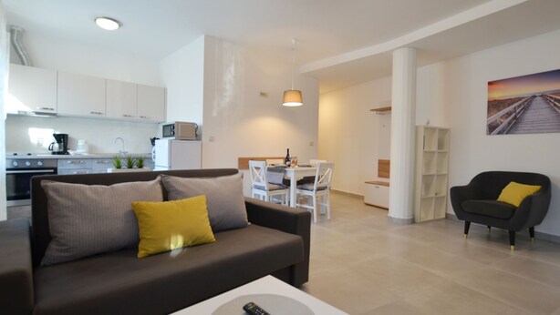 A modern living room with a sofa, a dining area, and a kitchen in the background. - Stylish and Modern Rovinj Apartment (Rovinj)