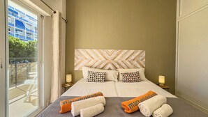 A hotel room with a large bed, two bedside tables, a patterned headboard, and a view of a balcony with outdoor furniture.