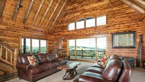 L’intérieur d’une cabane en rondins est aménagé avec un ensemble de canapés en cuir, une table basse en bois et une grande fenêtre qui offre une vue sur l’extérieur.