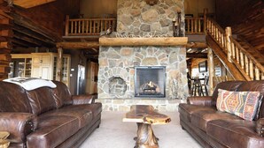 L’intérieur d’un chalet rustique, avec une cheminée en pierre, des canapés en cuir et un escalier en bois.