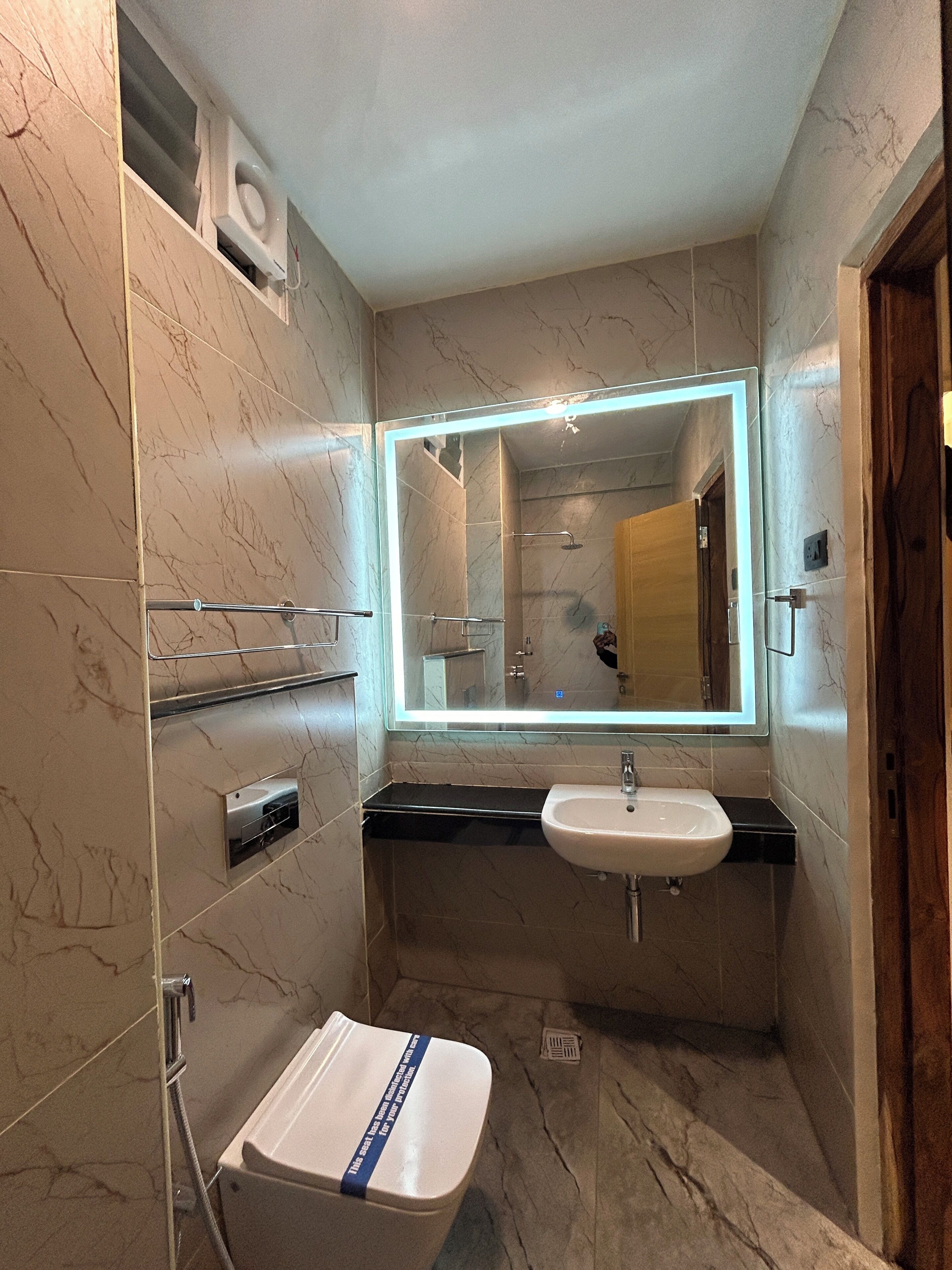 Une salle de bain compacte avec un lavabo blanc, un miroir doté d’un éclairage intégré et un espace douche.