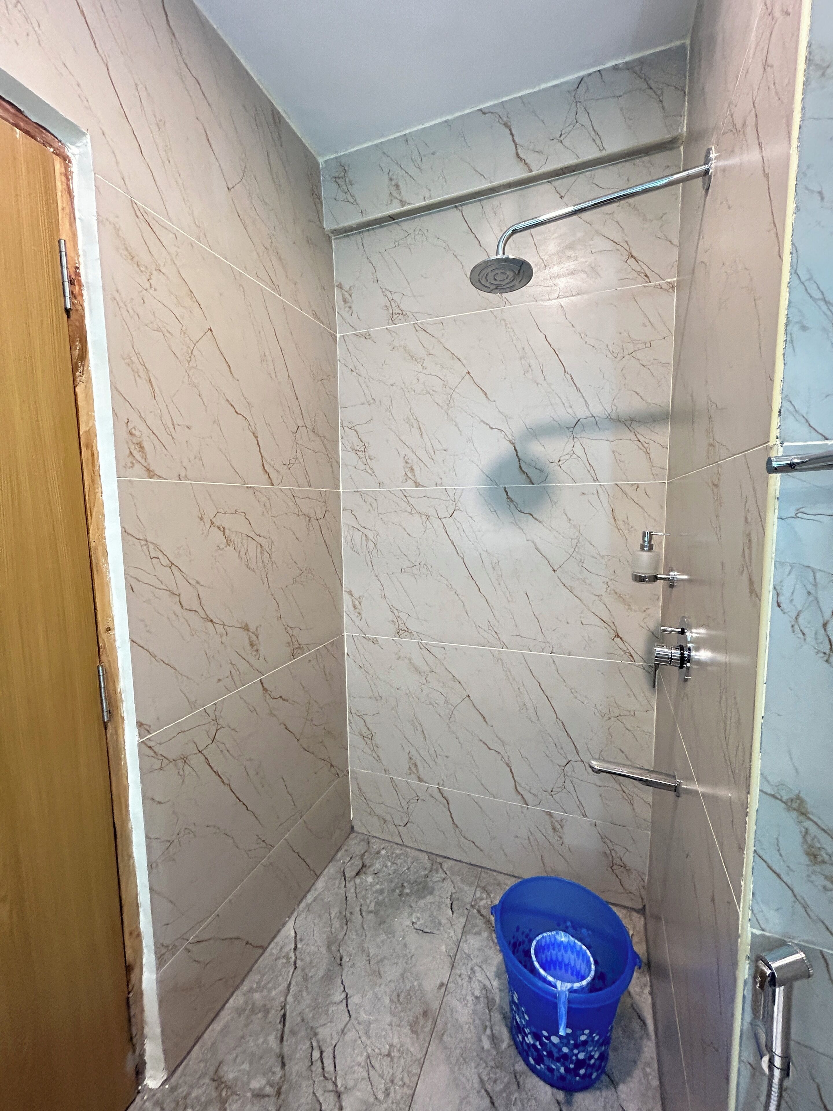 A small, enclosed shower area with a handheld showerhead, a blue bucket, and a door.