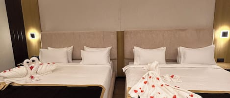 A hotel room with two beds, each with a headboard, white bedding, and a decorative towel arrangement.