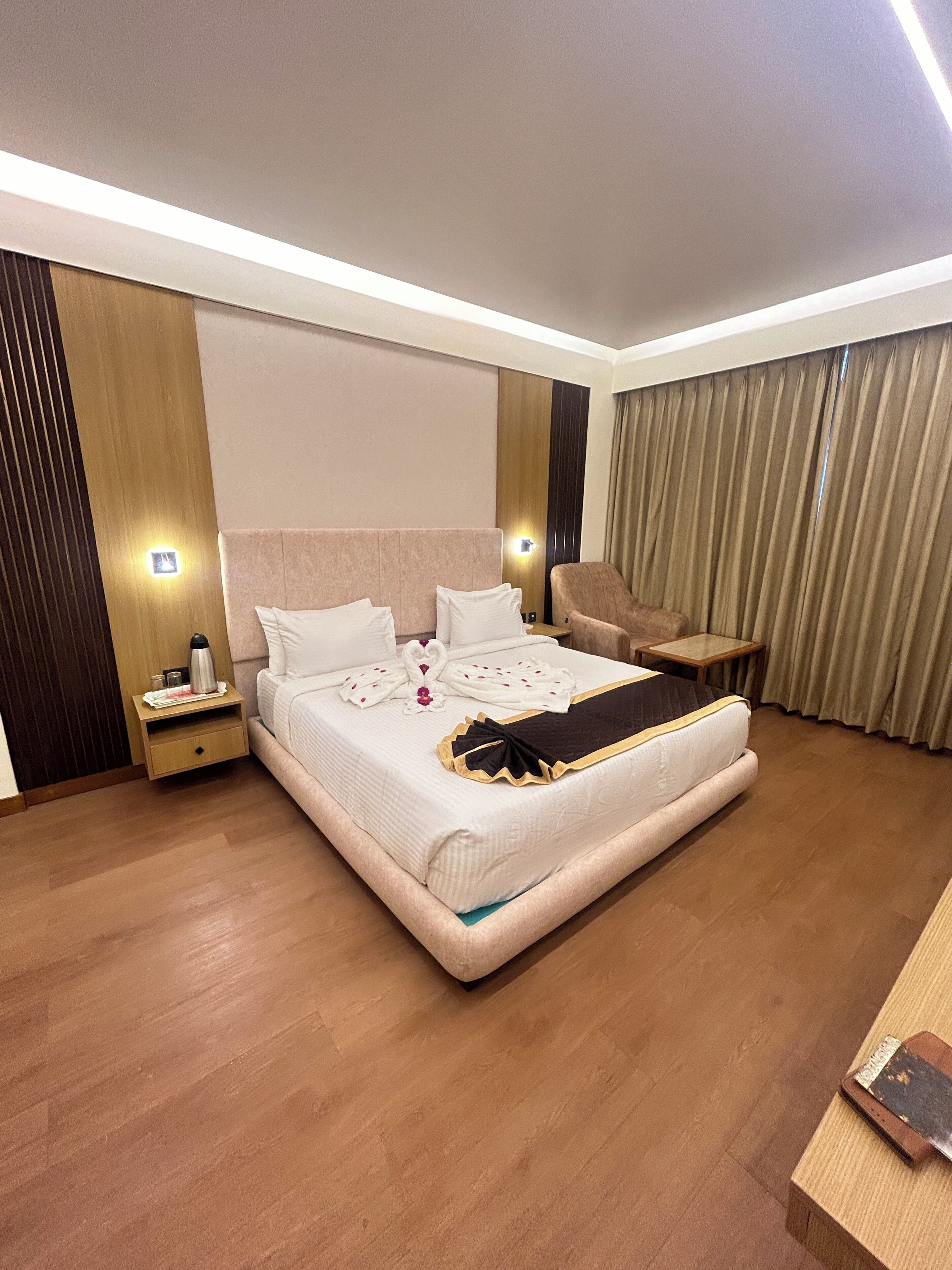 A modern hotel room with a large bed, bedside tables, a chair, and a desk.