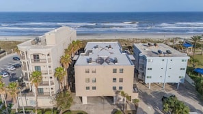 Un hotel frente a la playa con varias edificaciones, un estacionamiento y vistas al océano.