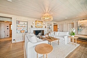 A spacious living room with a fireplace, white sofas, a coffee table, and a chandelier.