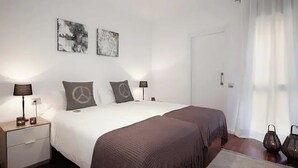 Un dormitorio con una cama grande, dos mesitas de noche con lámparas, una puerta y una ventana con cortinas.