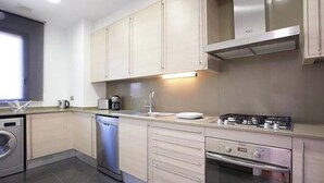 Una cocina moderna con armarios de tonos claros, lavavajillas integrado, estufa y pileta.