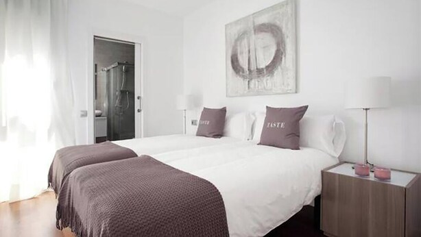 Habitación de hotel con una cama grande, dos mesitas de noche, una lámpara de noche, ducha y una obra de arte colgada en la pared.