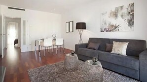 Una sala de estar moderna con un sofá gris, una mesa de centro y una zona de comedor con sillas blancas.