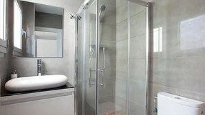 Un baño moderno con ducha de vidrio, lavamanos blanco y retrete.