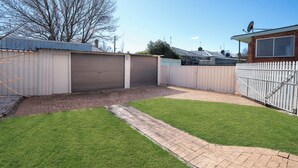 A fenced backyard with a paved path, a grassy area, and a garage. - Incredible Location! 2 Bed CBD Dream (Orange)