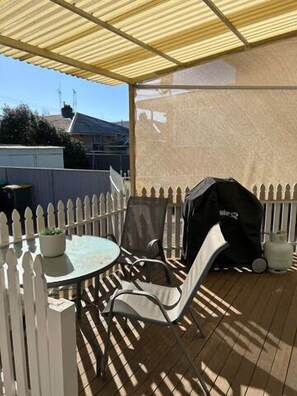 A covered patio with a round table and chairs, a white picket fence, and a barbecue grill. - Incredible Location! 2 Bed CBD Dream (Orange)