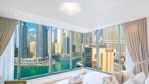 A modern hotel room with a large window offering a city view, a bed with white linens, and a hanging light fixture. - LUX  The Silverene Marina View Suite 4 (Dubai)