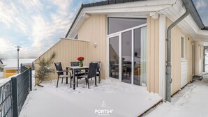 Ein überdachter Außenbereich mit Tisch und Stühlen, einer kleinen Pflanze und schneebedecktem Boden.