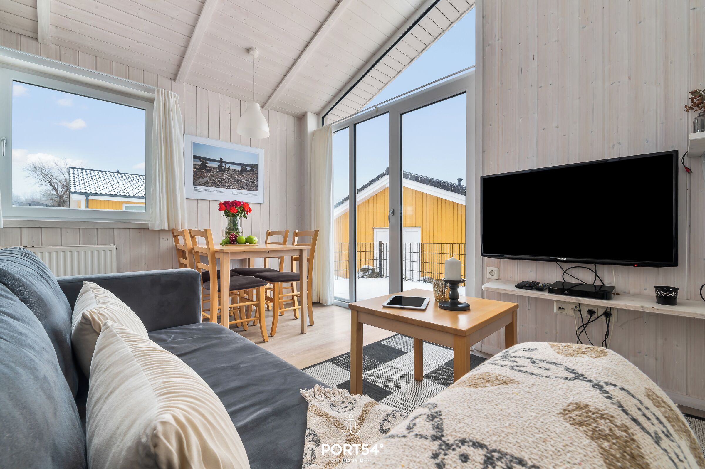 Ein modernes Wohnzimmer mit einer Couch, einem Tisch mit Fernseher und einem Essbereich mit Stühlen und Tisch.