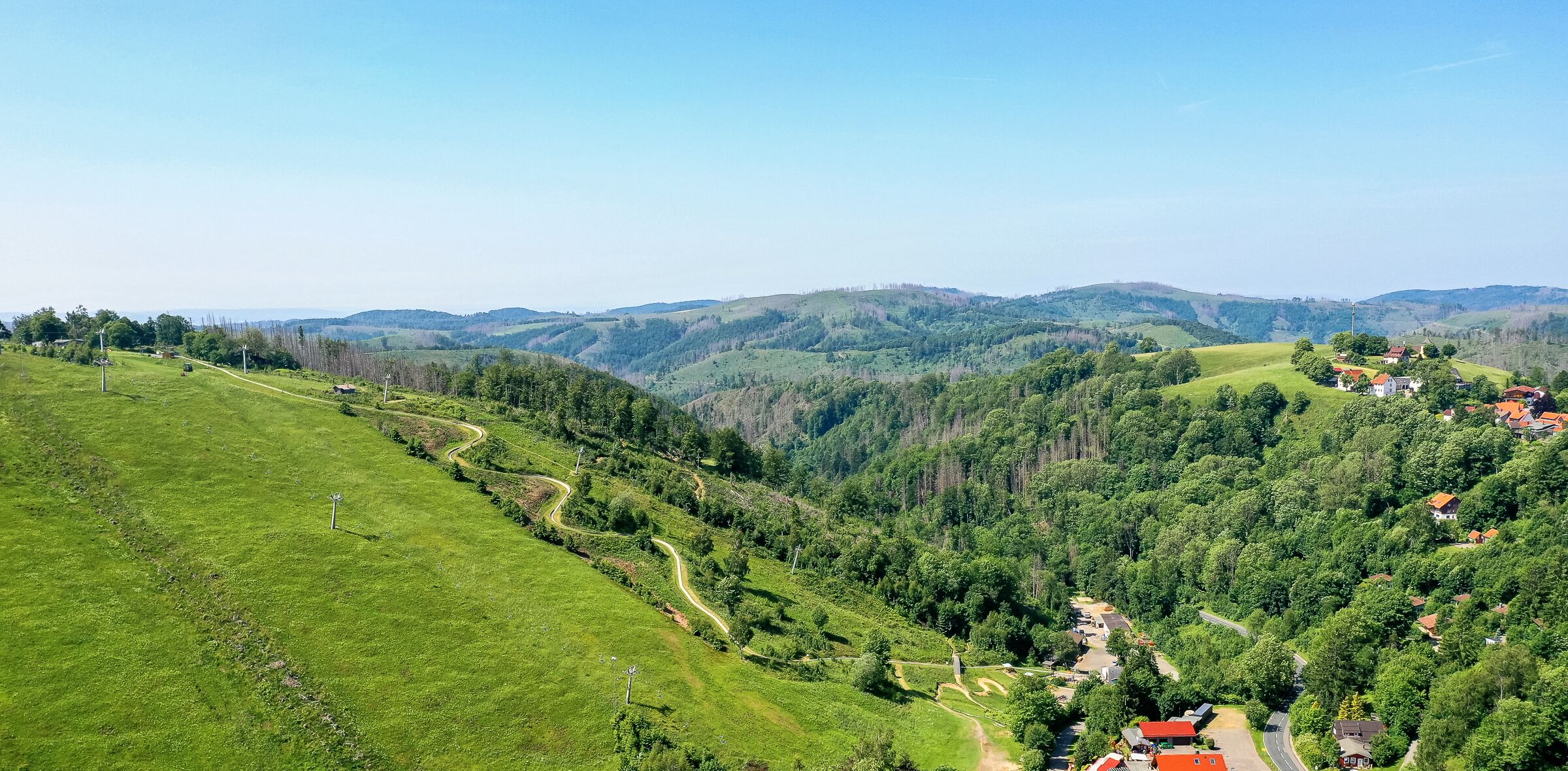 Ländliche Landschaft mit kurvenreichem Weg, grünen Feldern und verstreuten Häusern mit roten Dächern.