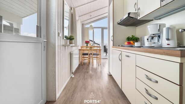 Une cuisine moderne avec des meubles en bois, un coin repas comprenant une table et des chaises, et une vue sur l’extérieur grâce à une porte ouverte.