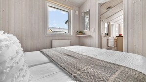 Une chambre avec un grand lit, une fenêtre donnant sur un beau paysage, un miroir et une étagère avec des plantes.