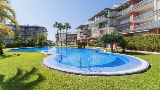 A modern apartment complex with a central swimming pool surrounded by well-maintained grass and palm trees. - Happy  - Apartment In Urbanització Platja D'oliva (Oliva Nova, Valencia)