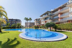 Un immeuble d’appartements moderne doté d’une piscine centrale, entourée de pelouses bien entretenues et de palmiers.