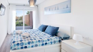 A bedroom with a bed, a nightstand, a painting, and a view of the outdoors. - Happy  - Apartment In Urbanització Platja D'oliva (Oliva Nova, Valencia)
