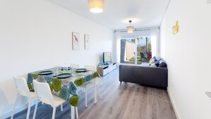 A modern dining area with a table set for four, white chairs, and a sofa in the background. - Happy  - Apartment In Urbanització Platja D'oliva (Oliva Nova, Valencia)