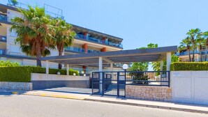 A modern hotel entrance with a covered walkway, palm trees, and a clear blue sky. - Happy  - Apartment In Urbanització Platja D'oliva (Oliva Nova, Valencia)
