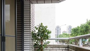Un balcón con una planta en maceta, suelo de baldosas y vista de edificios al fondo.