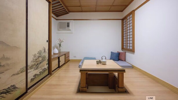 Una habitación japonesa tradicional con suelo de tatami, una mesa baja con tetera, un sofá con cojines, un divisor shoji y vistas a un paisaje montañoso.