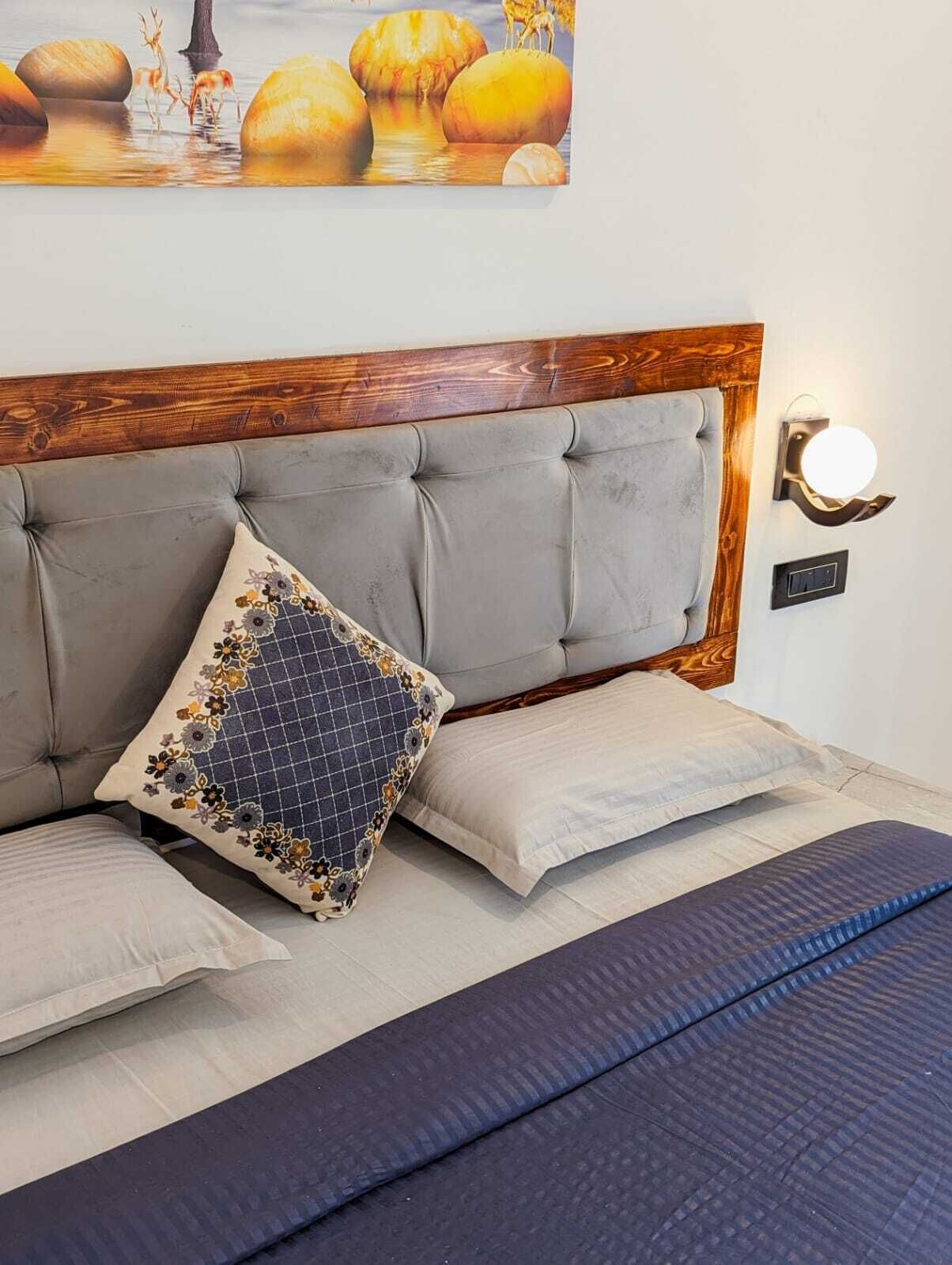 A bedroom with a tufted headboard, a bed with a patterned pillow, a wall-mounted light, and a painting above the bed.