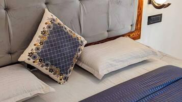 Un dormitorio con cabecera capitonada, cama con almohada estampada, luz adosada a la pared y un cuadro sobre la cama.