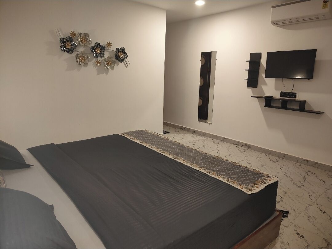Une chambre à coucher comprenant un lit, un téléviseur fixé au mur, un miroir et un élément décoratif mural.