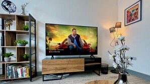 Un saló amb una televisió que mostra un pòster de pel·lícula, una prestatgeria amb llibres, una taula de centre amb un vas i una làmpada.
