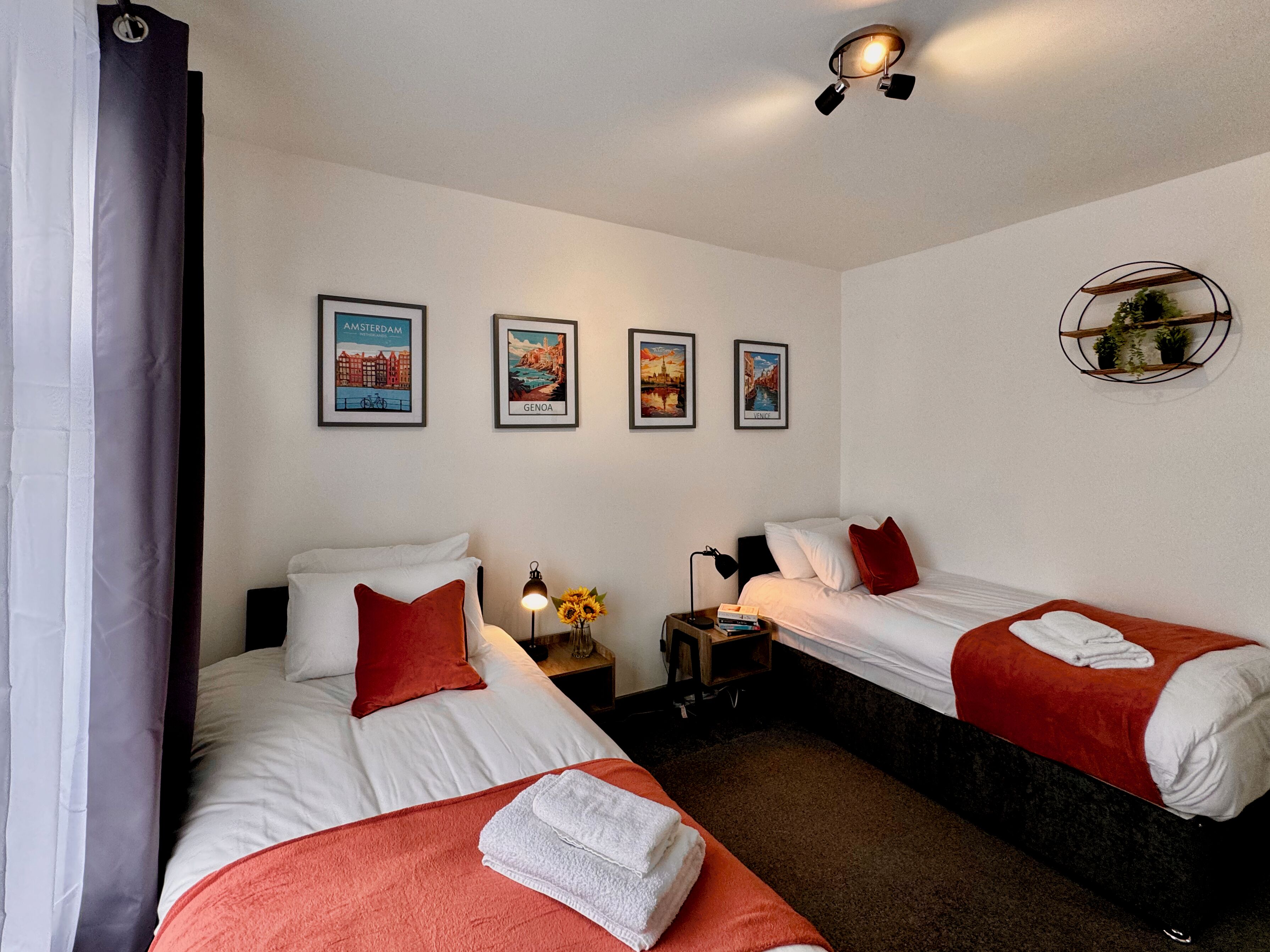 A hotel room with two beds, a nightstand, a lamp, and wall-mounted pictures of Amsterdam, Genoa, and Venice.