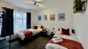 Habitació d'hotel amb dos llits, una finestra amb cortines, un ventilador de sostre i quadres a la paret.