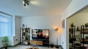 Un saló modern amb una televisió de pantalla plana, una biblioteca, una taula de centre i una catifa colorida.