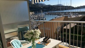 A balcony with a table, a chair, a vase of flowers, and a view of a marina with boats and buildings in the background.