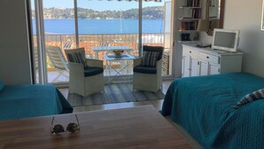 A room with two beds, a desk with a computer, a chair, a table, and a view of the sea.