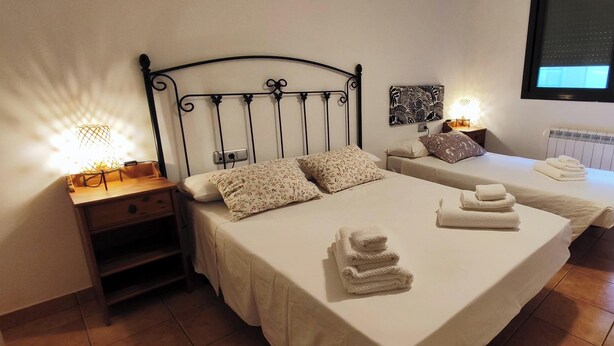 A hotel room with two beds, a nightstand with a lamp, a radiator, and a window with blinds. - RURAL APARTMENT SOL BERGUEDA (Avià Barcelona)