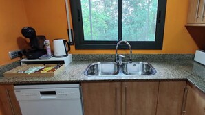 A kitchen with a double sink, a coffee maker, a toaster, and a window with a view of trees. - RURAL APARTMENT SOL BERGUEDA (Avià Barcelona)