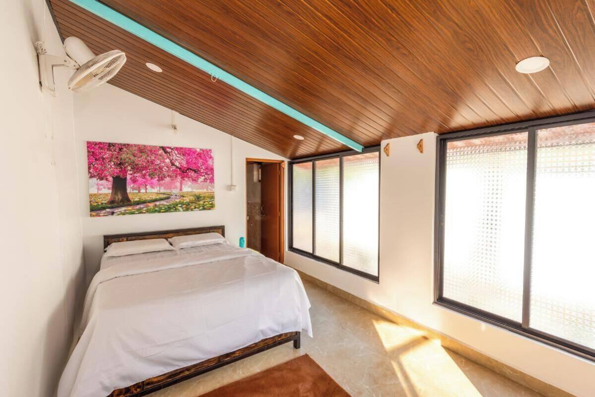 Un dormitorio con cama, un ventanal con persianas, un ventilador de techo y un cuadro de un árbol.