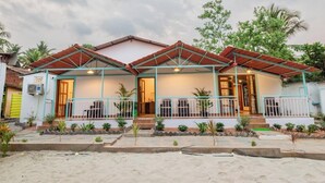 A two-story house with a tiled roof, a porch with a railing, and a small garden area. - Olive Beach House (Canacona)