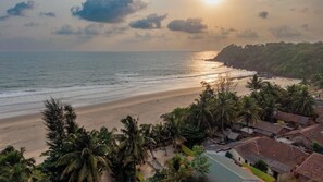 A beach with a row of houses, palm trees, and a sunset. - Olive Beach House (Canacona)