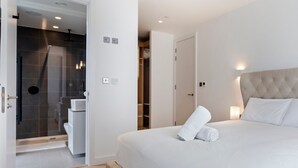 A modern bedroom with a large bed, a walk-in closet, and a shower area. - Stylish Flat-Leisure Pool & Gym (Greater London)