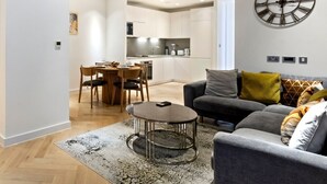 A modern living room with a grey sofa, a coffee table, and a dining area with wooden chairs. - Stylish Flat-Leisure Pool & Gym (Greater London)