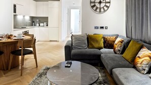 A modern living room with a grey sofa, a round coffee table, and a large wall clock. - Stylish Flat-Leisure Pool & Gym (Greater London)