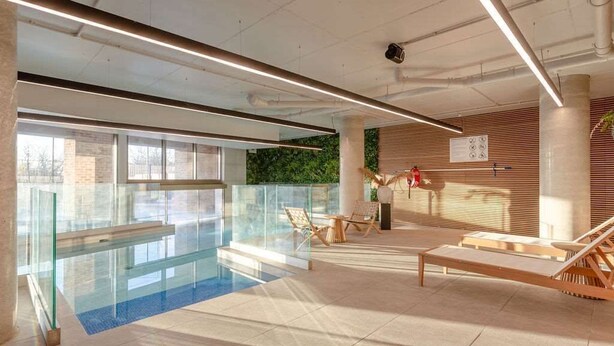 A modern indoor pool area with glass railings, lounge chairs, and a view of the outdoors. - Stylish Flat-Leisure Pool & Gym (Greater London)