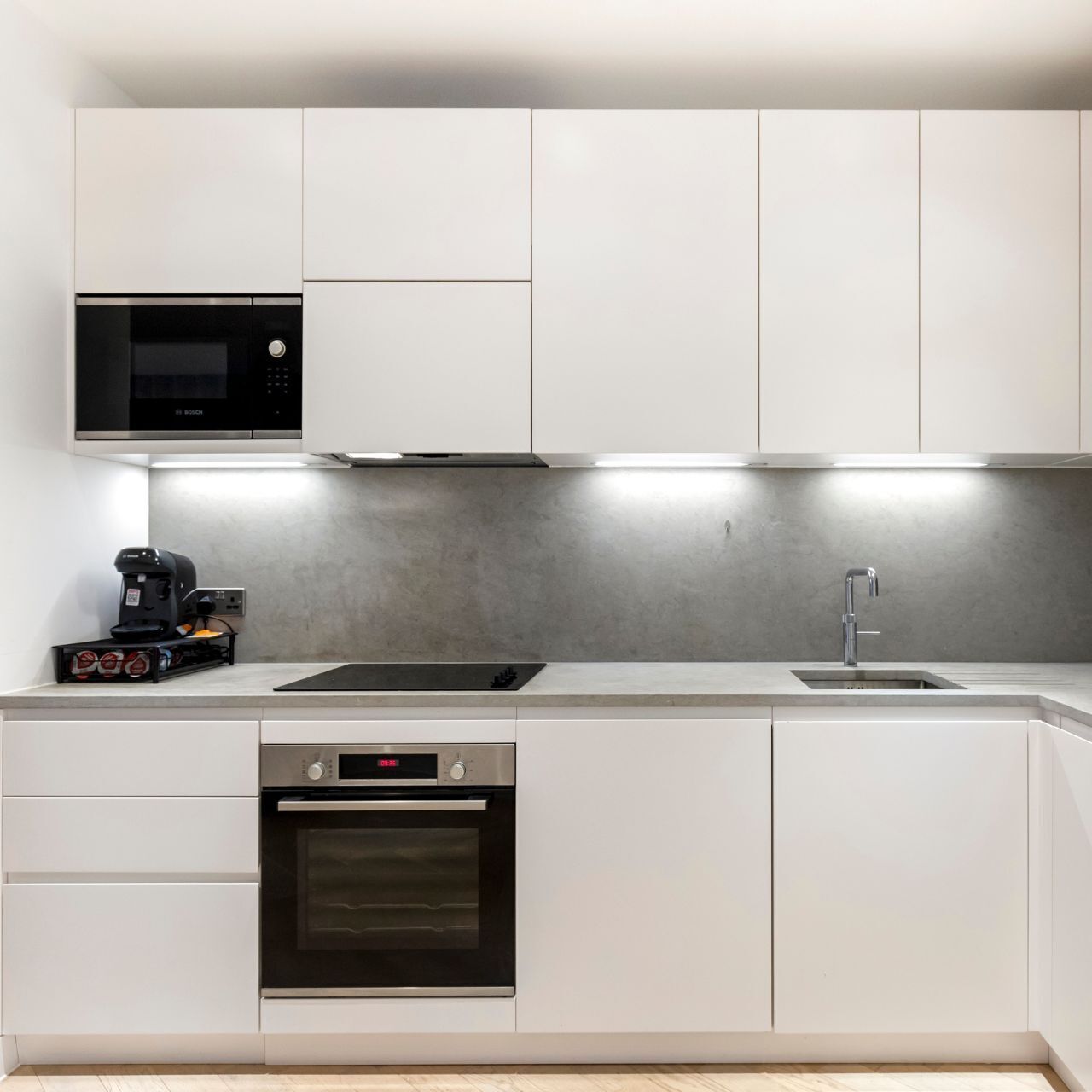 A modern kitchen with white cabinets, a black Bosch microwave, a coffee machine, a sink, and a built-in oven.