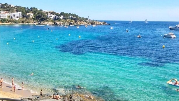 A coastal scene with clear turquoise waters, boats, and a sandy beach.